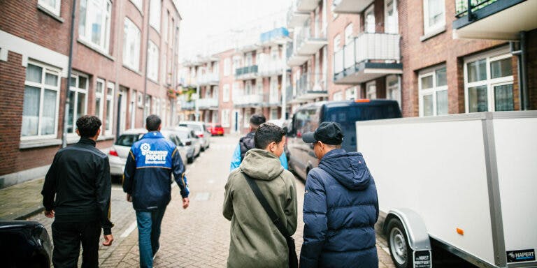 Photo from behind of a group of kids walking together along a street in the Bloemhof neighbourhood of Rotterdam. The street is lined with 3-storey brick buildings