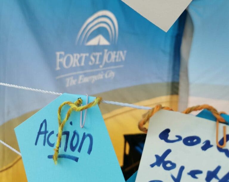 close up photo of an engagement event in Fort St. John. In the front, there are two sticky notes that people have written their priorities on. One says "Action". In the back, there is a blurred Fort St John logo